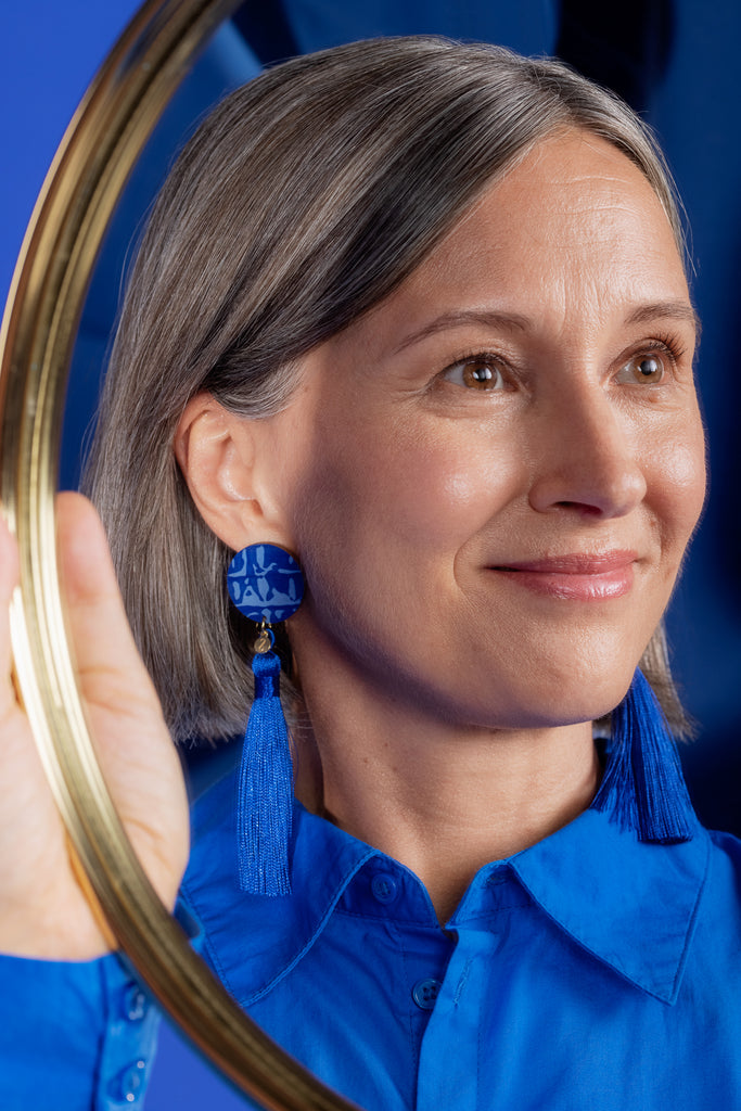 Siniset Sinua Forever Dreaming-puukorvakorut tasseleilla ja pienellä logoriipuksella, mallin päällä.